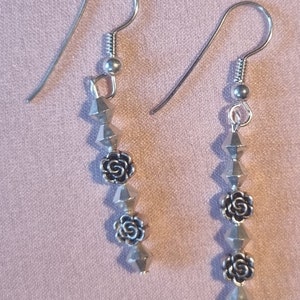 May include: Silver dangle earrings with a series of silver beads and rose-shaped charms.