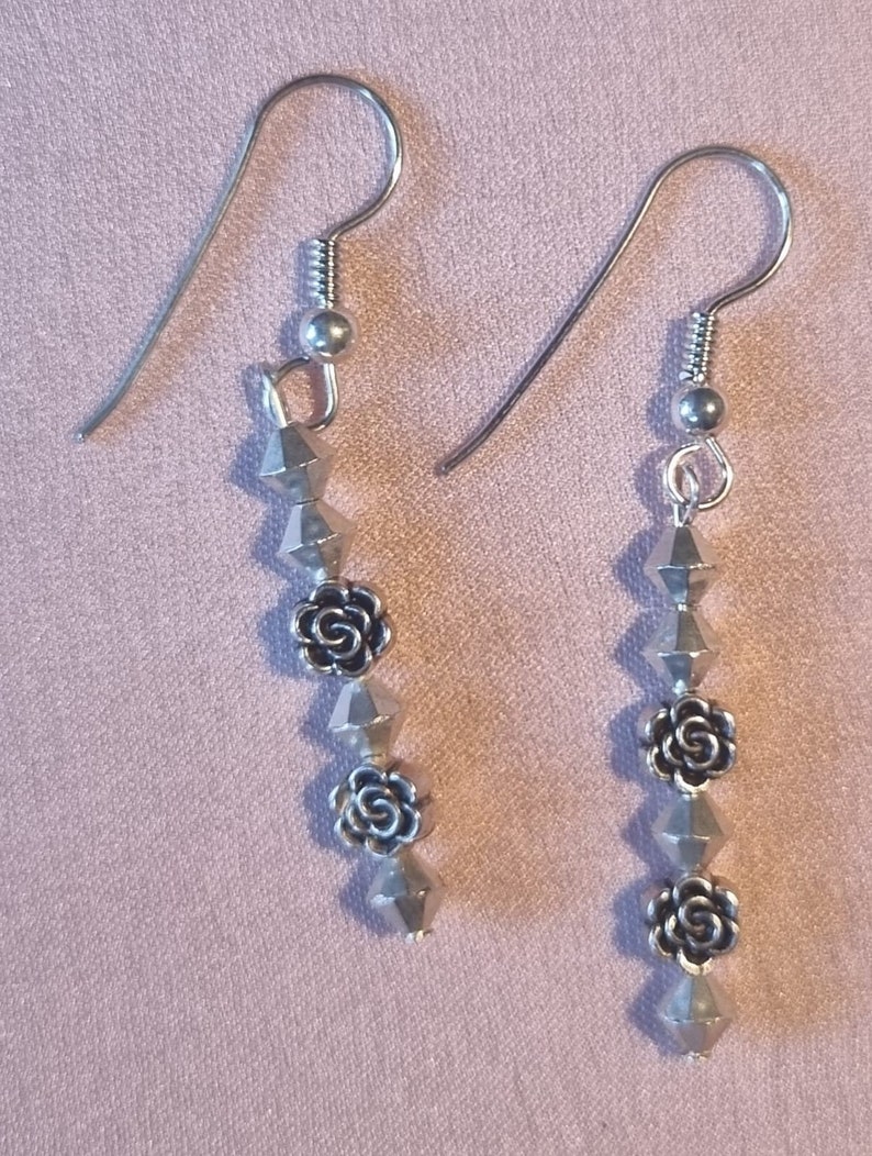 May include: Silver dangle earrings with a series of silver beads and rose-shaped charms.