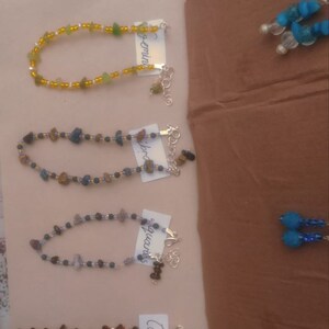 May include: Four bracelets made with different colored beads and stones, each with a tag labeled with a zodiac sign: Gemini, Libra, Aquarius, and Capricorn.