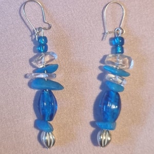 May include: A pair of dangle earrings featuring blue and clear glass beads with silver accents.