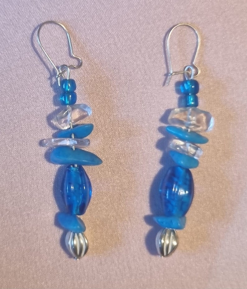 May include: A pair of dangle earrings featuring blue and clear glass beads with silver accents.