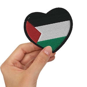 Puede incluir: Un parche en forma de corazón con los colores de la bandera palestina: negro, blanco, rojo y verde. El parche se sostiene en una mano.