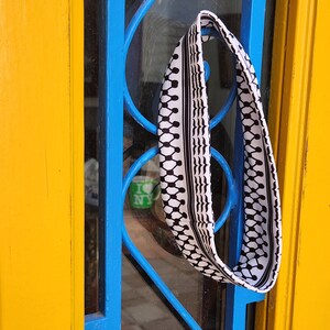 May include: A black and white patterned headband hanging on a blue metal door frame against a yellow door.