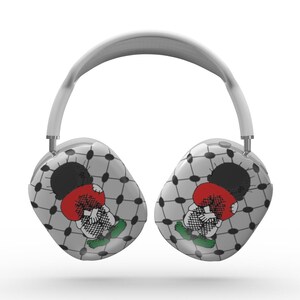 Pode incluir: Fones de ouvido brancos over-ear com uma faixa de cabeça e fones de ouvido acolchoados. Os fones de ouvido apresentam um design de personagem de desenho animado com um esquema de cores preto, vermelho e verde, em um padrão geométrico cinza e branco. Os fones de ouvido são projetados para ouvir áudio.