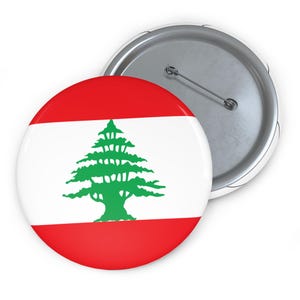 May include: A round button featuring the flag of Lebanon. The design includes a green cedar tree on a white background, bordered by red stripes.