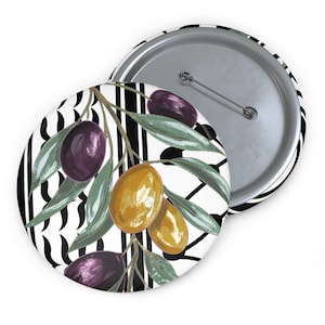 May include: A round button with a graphic of olives and leaves on a black and white striped background. The olives are purple and yellow, and the leaves are green. The button has a metal pin back.
