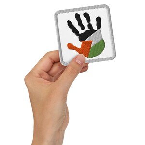 May include: Square embroidered patch featuring a handprint design. The handprint is colored with the Palestinian flag: black, white, green, and red. The patch has a white background and a gray border. The patch is held in a person's hand.