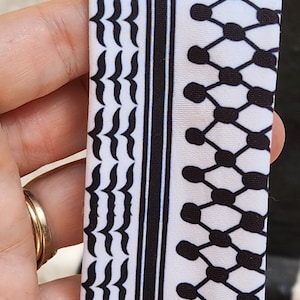 May include: A white fabric with a black and white geometric pattern. The pattern features a repeating design of small black circles and a wavy line.