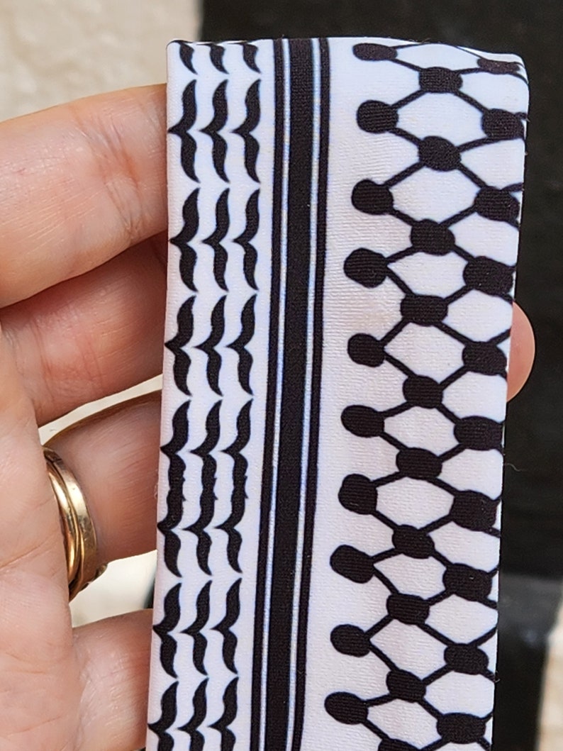 May include: A white fabric with a black and white geometric pattern. The pattern features a repeating design of small black circles and a wavy line.