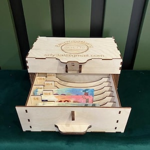 May include: Wooden box with a drawer for storing cash. The box has slots for bills of different denominations, including 5 euro, 10 euro, 50 euro, 100 euro, and 200 euro. The box is labeled "Easy Wood Making" and includes the email address "sdy3al@gmail.com".