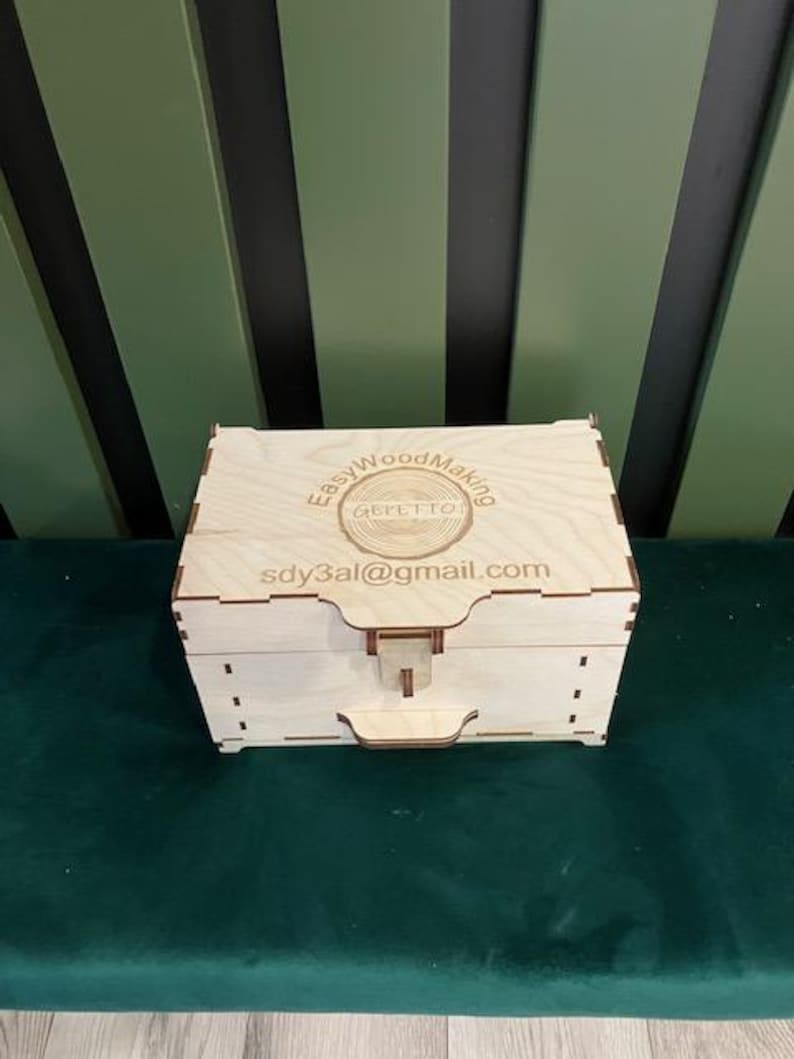 May include: A wooden box with a hinged lid and a latch. The box is engraved with the text "Easy Wood Making" and a logo. The text "sdy3al@gmail.com" is also engraved on the box.