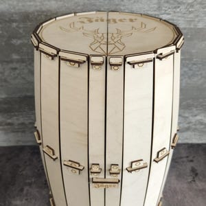 Puede incluir: Una caja de madera con forma de barril con una tapa con bisagras. La tapa está decorada con un diseño de cabeza de ciervo cortado con láser y la palabra "Jager".