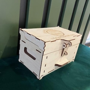 May include: A wooden box with a hinged lid and a latch. The box is made of light wood and has a circular design on the top. The text "Ship Galore" is engraved on the box.