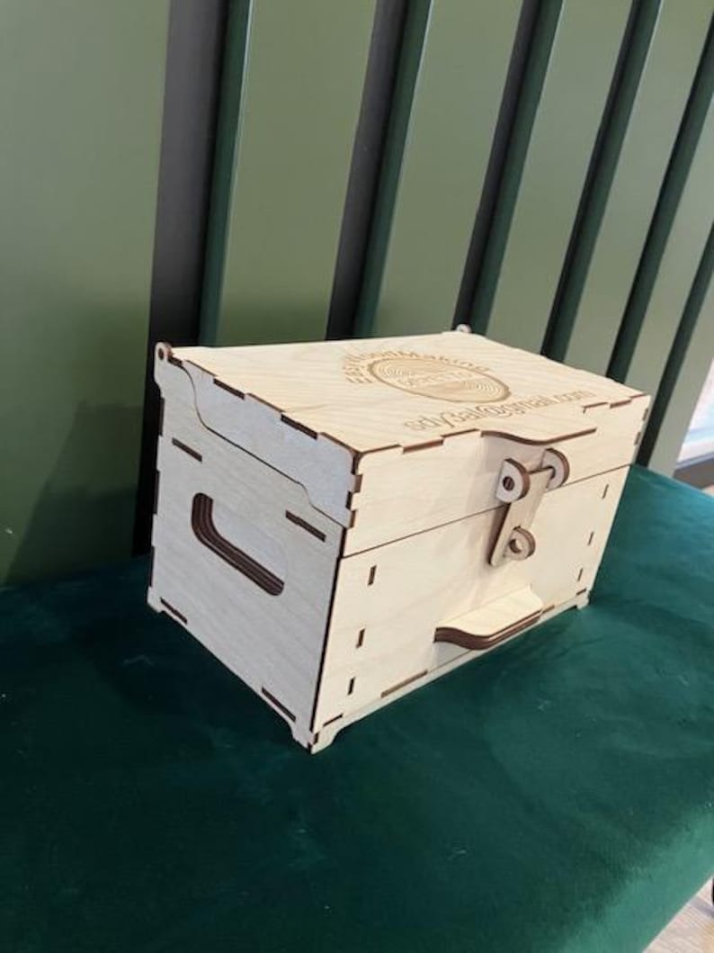 May include: A wooden box with a hinged lid and a latch. The box is made of light wood and has a circular design on the top. The text "Ship Galore" is engraved on the box.
