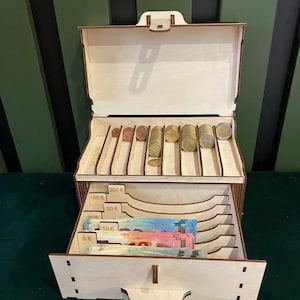 May include: Wooden cash box with a drawer and compartments for organizing coins and bills. The box has labels for different denominations of Euro currency, including 5 Euro, 10 Euro, 20 Euro, 50 Euro, 100 Euro, and 200 Euro.