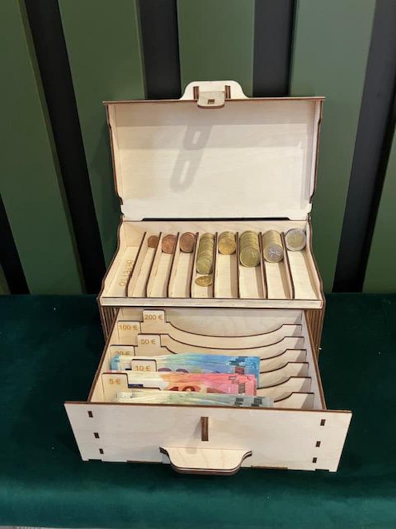 May include: Wooden cash box with a drawer and compartments for organizing coins and bills. The box has labels for different denominations of Euro currency, including 5 Euro, 10 Euro, 20 Euro, 50 Euro, 100 Euro, and 200 Euro.