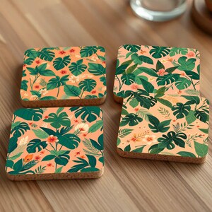 May include: Four square cork coasters with a tropical leaf and flower pattern on a light brown wooden surface.