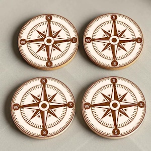 May include: Set of four brown wooden coasters with a white compass design. Each coaster features a compass rose with the letters N, S, E, and W.