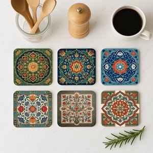 Puede incluir: Seis posavasos cuadrados con intrincados diseños florales y geométricos en tonos azules, verdes, rojos y dorados. Los posavasos están dispuestos sobre una superficie blanca, junto con una taza de café, cucharas de madera y un molinillo de pimienta.