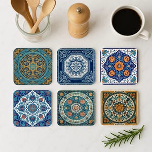 Può includere: Sei sottobicchieri quadrati con motivi intricati e colorati. I disegni includono motivi floreali e geometrici nei toni del blu, dell'oro e dell'arancione. Alcuni sottobicchieri hanno la scritta "ANTALYA". Sono visibili anche una tazza di caffè, cucchiai di legno e un macina spezie.