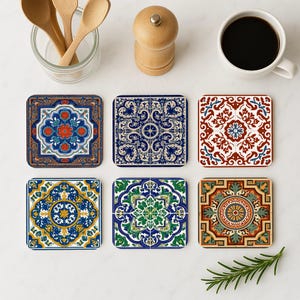Pode incluir: Seis bases de copos quadradas com desenhos de azulejos intrincados e coloridos. As bases de copos apresentam padrões em tons de azul, vermelho, verde e dourado. Uma xícara de café, colheres de madeira, um moedor de pimenta e um raminho de alecrim também são visíveis.