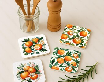 Op de afbeelding: Vier vierkante onderzetters met een aquarelontwerp van sinaasappels, groene bladeren en witte bloesems. Houten keukengerei in een glazen pot, een houten pepermolen en een takje rozemarijn zijn ook aanwezig.