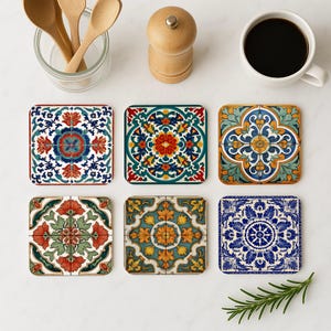 May include: Six square ceramic coasters with detailed floral patterns in red, blue, green, yellow, and white. The coasters are arranged on a white surface. A cup of coffee, wooden spoons, and a pepper grinder are also visible. Each coaster has a unique design.