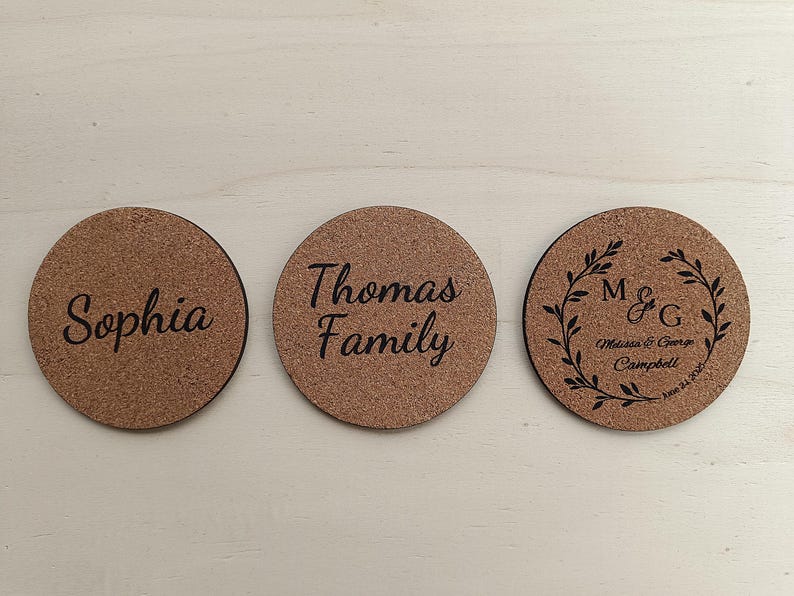A set of round cork coasters, each engraved with personalized text (e.g., names or monograms), displayed on a neutral surface. They highlight the option to customize the backside with any text you choose