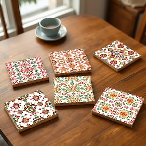 May include: Six square-shaped coasters with intricate floral patterns in shades of red, green, orange, and white. The coasters are made of ceramic and have a cork backing.