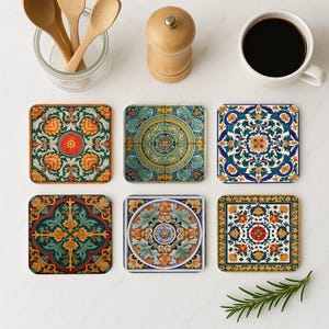May include: Six square coasters with intricate floral and geometric designs in various colors, including orange, green, blue, and yellow. The coasters are arranged on a white surface, alongside a cup of coffee, wooden spoons, and a pepper grinder.