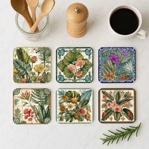 May include: Six square coasters with botanical designs. Each coaster features a different floral and foliage arrangement in shades of green, yellow, pink, and purple. The coasters are arranged on a white surface, with a cup of coffee and kitchen utensils.