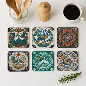 May include: Six square ceramic coasters with intricate, colorful designs. The coasters feature peacock, crane, and dragon motifs in shades of blue, green, orange, and yellow. The coasters are arranged on a white surface, alongside a cup of coffee and kitchen utensils.