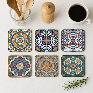 Könnte beinhalten: Sechs quadratische Untersetzer mit farbenfrohen, aufwendigen Blumen- und geometrischen Mustern in Blau-, Grün-, Gelb- und Orangetönen. Die Untersetzer sind auf einer weißen Oberfläche angeordnet, zusammen mit einer Kaffeetasse, Holzlöffeln und einer Pfeffermühle.