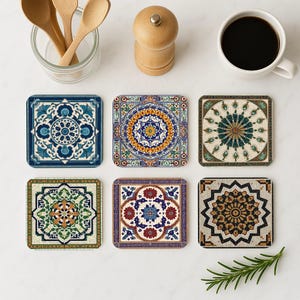 May include: Six square coasters with intricate, colorful mosaic tile designs. The coasters feature patterns in shades of blue, orange, green, and brown. A cup of coffee, wooden spoons, and a pepper grinder are also visible.