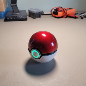 May include: A red and white Poke Ball with a glowing green button. The Poke Ball is a popular collectible toy from the Pokemon franchise.