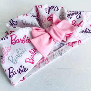 May include: A white headband with a pink bow and the word "Barbie" printed in various colours and fonts.