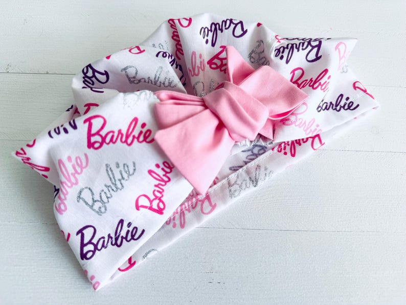 May include: A white headband with a pink bow and the word "Barbie" printed in various colours and fonts.