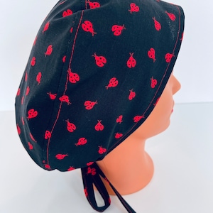 May include: Black scrub hat with a red ladybug print. The hat has a tie at the back.