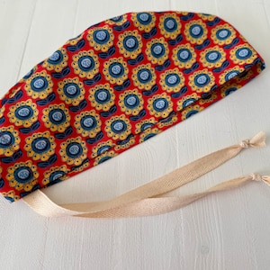 May include: A red scrub cap with a yellow and blue floral pattern and two long, cream-colored ties.