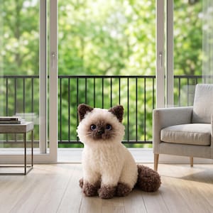 May include: A plush stuffed cat toy with cream-colored fur on the body and dark brown fur on the ears, face, and paws. The toy has large, round, dark blue eyes, a small black nose, and a textured, curly appearance throughout its soft exterior.