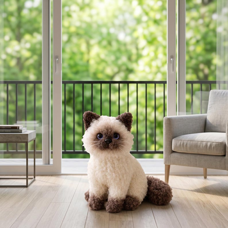 May include: A plush stuffed cat toy with cream-colored fur on the body and dark brown fur on the ears, face, and paws. The toy has large, round, dark blue eyes, a small black nose, and a textured, curly appearance throughout its soft exterior.