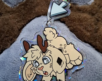 May include: A clear acrylic keychain featuring a cartoon-style fawn with large eyes, antlers, and a diamond-shaped marking. The keychain has a silver clasp and a holographic border. The fawn is light brown with black accents.