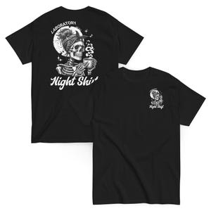 Könnte beinhalten: Schwarze T-Shirts mit einer weißen Grafik eines Skeletts mit Kopftuch, das eine Tasse hält, und den Worten "Laboratory Night Shift". Eine kleinere Grafik befindet sich auf dem anderen Shirt.