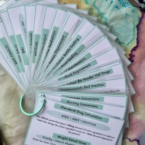 May include: A set of green and white flashcards with medical terms and calculations. The cards are fanned out and have a ring to hold them together.
