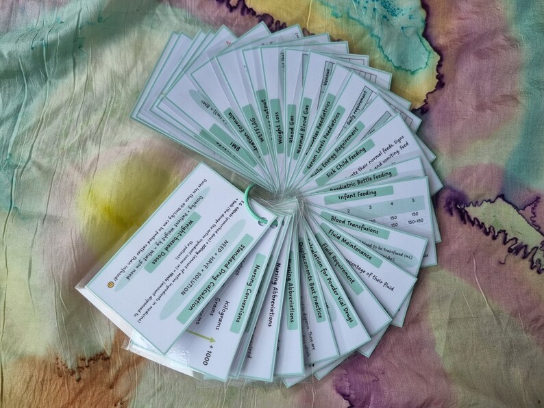 May include: A set of green and white flashcards with medical terms and calculations. The cards are fanned out in a circle, with the text facing outward. The cards include terms such as "Standard Drug Calculation", "Fluid Maintenance", "Nursing Abbreviations", and "Weight-based Doses".