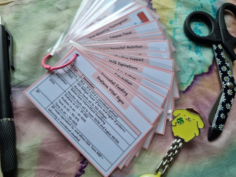 May include: A set of pink-edged flashcards with medical information, including "Preterm Vital Signs" and parameters for temperature, heart rate, and respiration. A pen, scissors, and a yellow character pin are also visible.