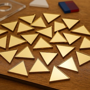 May include: A collection of small, gold-colored triangle-shaped objects arranged on a wooden surface. The triangles have a reflective, metallic appearance. Other geometric shapes are visible in the background.