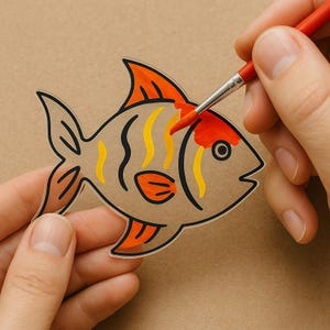 May include: A hand paints a clear plastic fish with orange and yellow stripes. The fish is being painted with red paint.