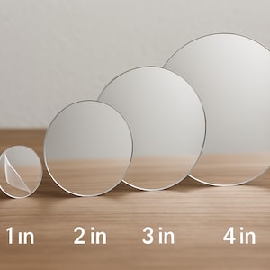 May include: Four clear, circular objects of varying sizes, ranging from 2.5 cm to 10 cm in diameter, are arranged on a wooden surface. The smallest object has a partially peeled sticker. The sizes are labeled with white text.