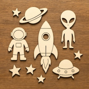 May include: Wooden space-themed cutouts including a rocket ship, astronaut, alien, planet with rings, stars, and a UFO. The cutouts are made of light-colored wood and are arranged on a wooden surface.